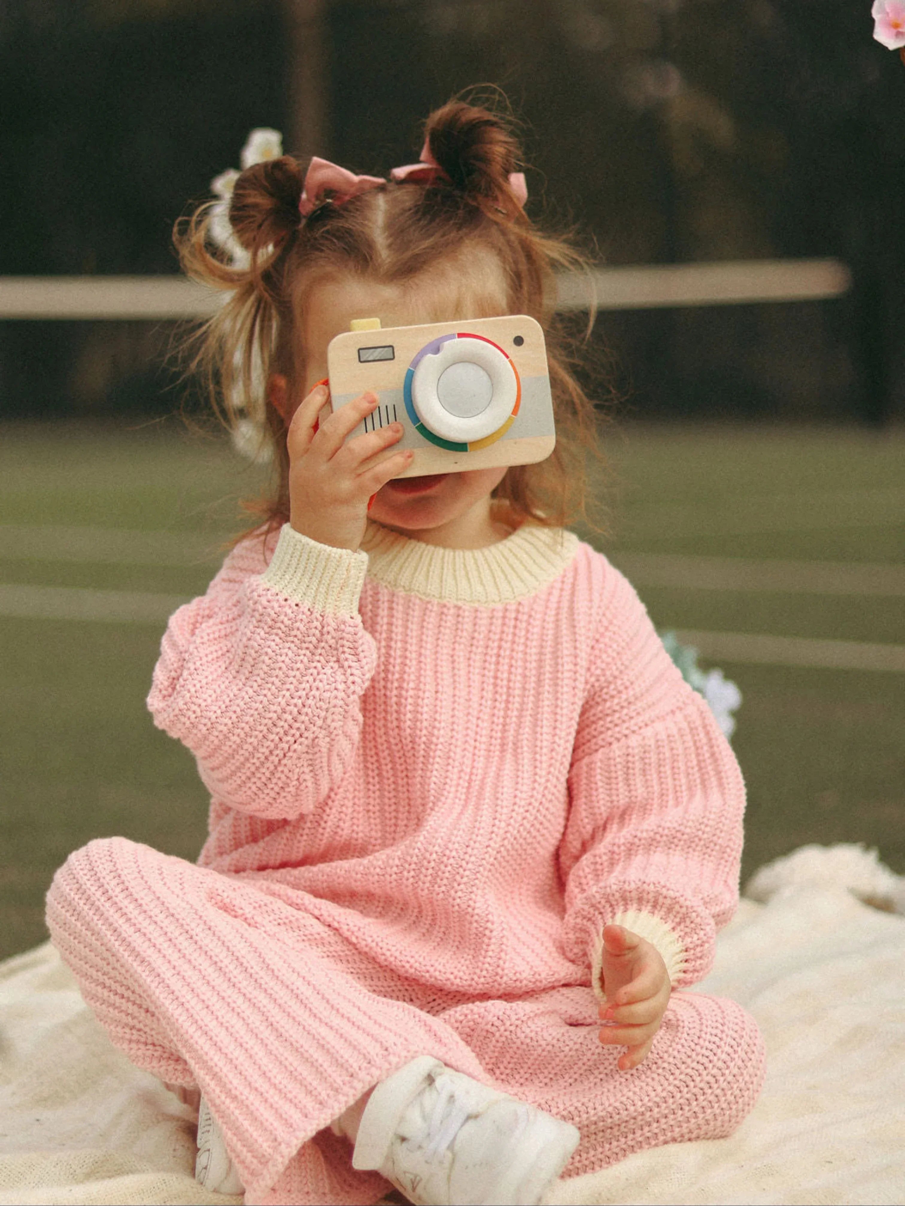 Child in pink outfit holding a toy camera outdoors