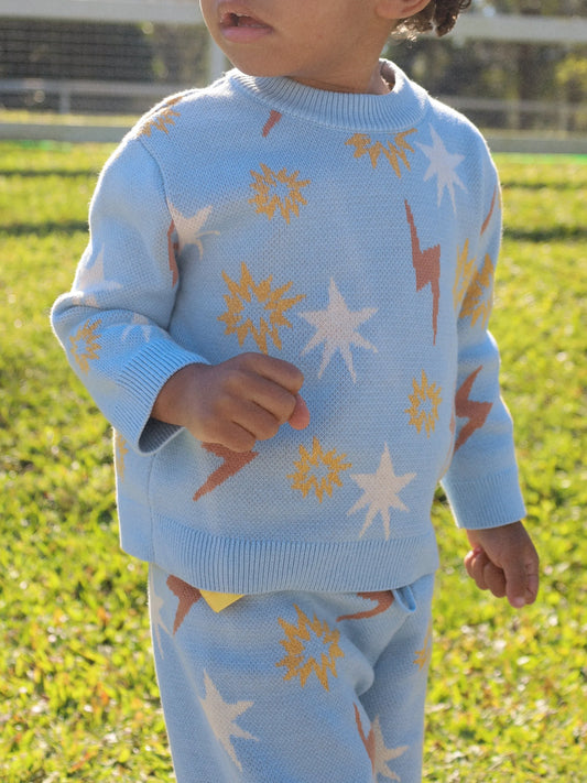 Child wearing a light blue sweater and pants with star and sun patterns outdoors.