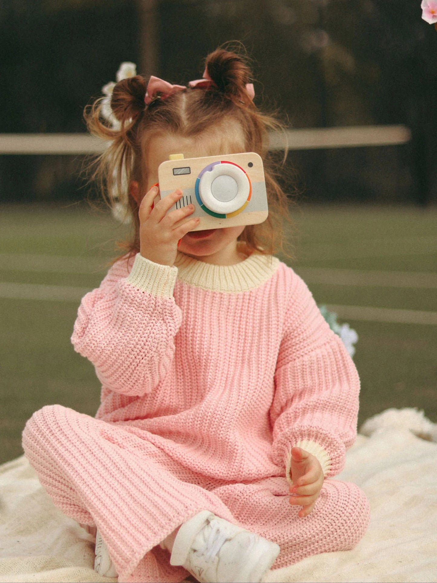 Child in pink outfit holding a toy camera outdoors