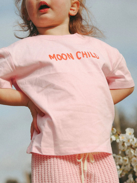 Child wearing a pink 'MOON CHILD' t-shirt with a blurred natural background