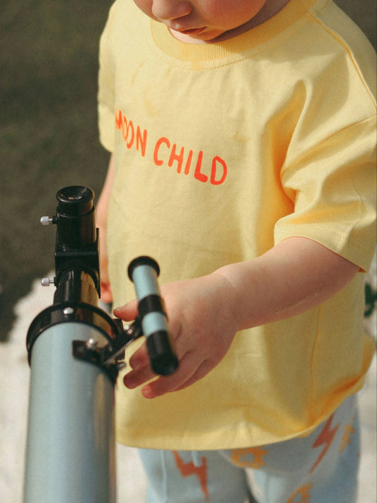 Child holding a telescope wearing a yellow shirt with 'MOON CHILD' text.